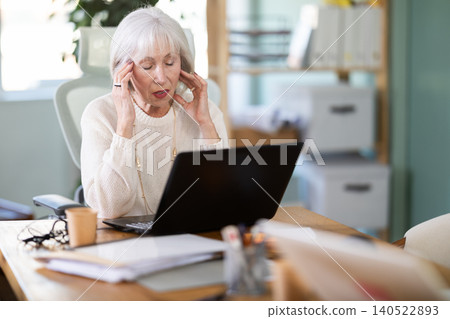 Elderly businesswoman suffers from headaches while working in office Elderly businesswoman suffers from headaches while working in office 140522893