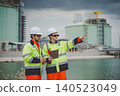 Field engineers in high visibility jackets pointing and discussing at coastal oil facility 140523049