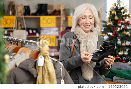 Positive old lady choosing heeled ankle boots in clothing store Positive old lady choosing heeled ankle boots in clothing store 140523051