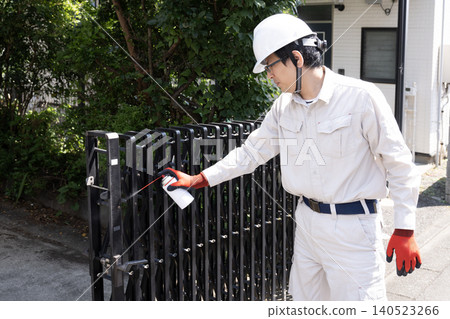 A worker sprays lubricant onto the retractable gate of a parking lot. A worker sprays lubricant onto the retractable gate of a parking lot. 140523266