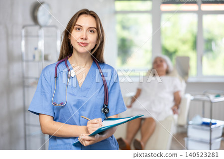 Female doctor in scrub holding clipboard. Female doctor in scrub holding clipboard. 140523281
