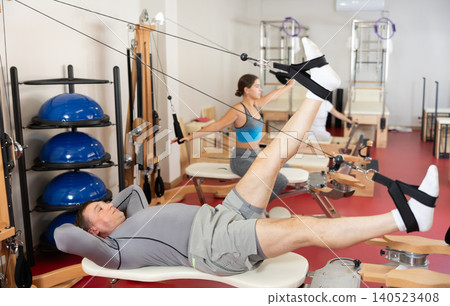 Man is engaged in Pilates simulator with cable and ropes for stretching leg muscles Man is engaged in Pilates simulator with cable and ropes for stretching leg muscles 140523408