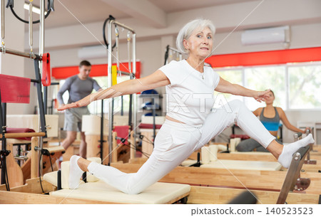 Senior woman performs exercise on reformer to improve coordination, balance, and posture Senior woman performs exercise on reformer to improve coordination, balance, and posture 140523523