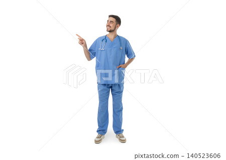 Doctor wearing blue medical scrubs points while smiling, on white Doctor wearing blue medical scrubs points while smiling, on white 140523606