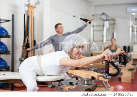 Elderly woman stretching her arms using pilates machine 140523753
