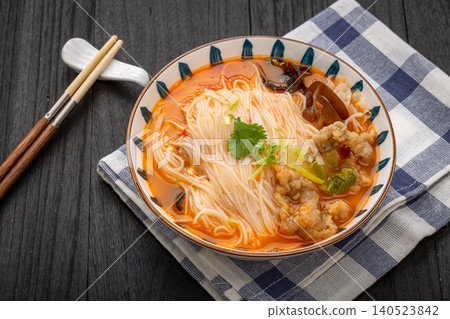 Spicy red soup noodles topped with crispy deep-fried pork, wood ear mushrooms, and chopsticks. 140523842