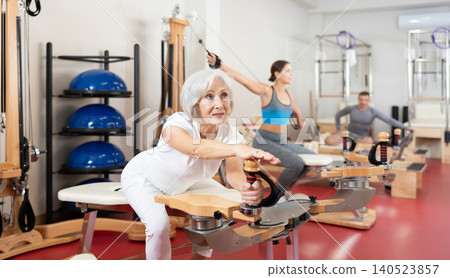 Elderly woman stretching her arms using pilates machine Elderly woman stretching her arms using pilates machine 140523857