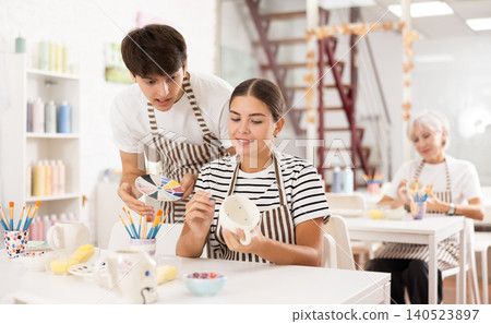 Young ceramicist teaching female novice art of ceramic painting in pottery studio Young ceramicist teaching female novice art of ceramic painting in pottery studio 140523897