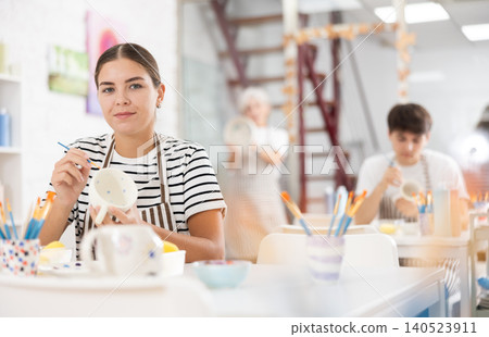Young female artist painting ceramic cup in pottery workshop 140523911