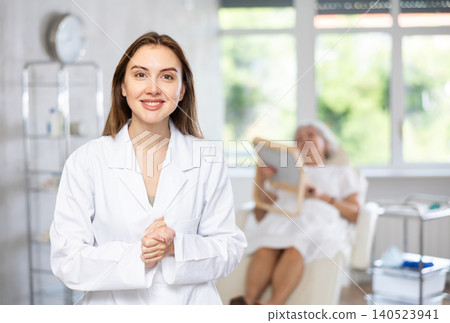 Female doctor cosmetologist stand with woman looking mirror behind in the doctors office. Female doctor cosmetologist stand with woman looking mirror behind in the doctors office. 140523941