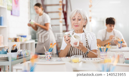 Experienced female artist painting ceramic cup in pottery workshop Experienced female artist painting ceramic cup in pottery workshop 140523955
