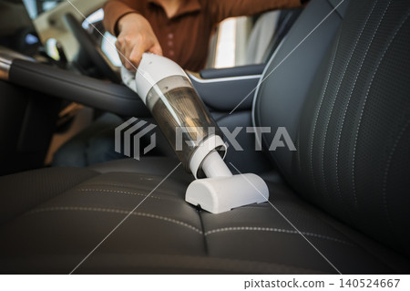 close up hand of woman using portable handheld vacuum cleaner to clean dust on leather car seat of electric car close up hand of woman using portable handheld vacuum cleaner to clean dust on leather car seat of electric car 140524667