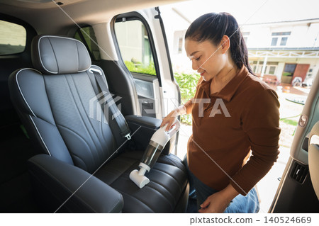 woman using portable handheld vacuum cleaner to clean dust on leather car seat of electric car 140524669