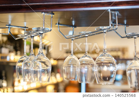 Empty Wine Glasses Hanging Upside Down on a Metal Rack Above a Bar Counter in a Modern Pub Empty Wine Glasses Hanging Upside Down on a Metal Rack Above a Bar Counter in a Modern Pub 140525568