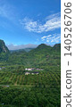 vertical panoramic view of lush green mountains covered by mist and low clouds above a rural village. 140526706