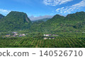 Panoramic view of lush green mountains covered by mist and low clouds above a rural village. 140526710