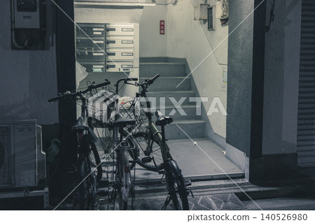 The entrance to a retro apartment building at night, with a bicycle and a shared staircase. The entrance to a retro apartment building at night, with a bicycle and a shared staircase. 140526980