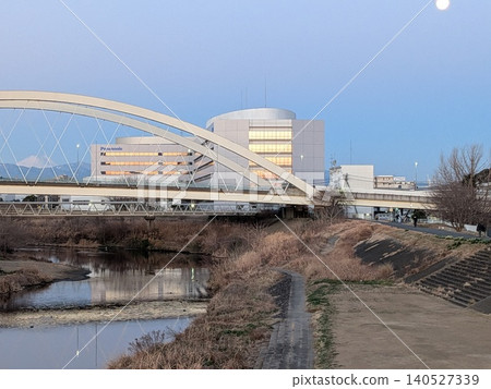 Winter twilight. Mount Fuji and the moon floating in the evening scenery of the Tama River, the arch bridge and the riverbank. Winter twilight. Mount Fuji and the moon floating in the evening scenery of the Tama River, the arch bridge and the riverbank. 140527339