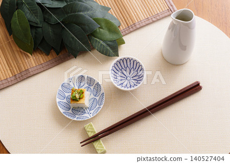 一張描繪日本料理的靜物照片,包括清酒和冰鎮豆腐 | 一張寧靜的餐桌照片,擺放著清酒瓶和神聖的樹枝。 一張描繪日本料理的靜物照片,包括清酒和冰鎮豆腐 | 一張寧靜的餐桌照片,擺放著清酒瓶和神聖的樹枝。 140527404