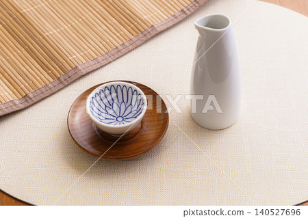 一張極簡主義的日式靜物攝影作品,畫面中是清酒和一瓶清酒放在木質杯墊上。 一張極簡主義的日式靜物攝影作品,畫面中是清酒和一瓶清酒放在木質杯墊上。 140527696