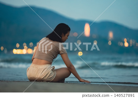 Woman sitting on shoreline beside sea waves during peaceful tropical evening by coast and playing with sand, Female traveler relaxing on sandy beach with ocean surf and calm seaside atmosphere Woman sitting on shoreline beside sea waves during peaceful tropical evening by coast and playing with sand, Female traveler relaxing on sandy beach with ocean surf and calm seaside atmosphere 140527891