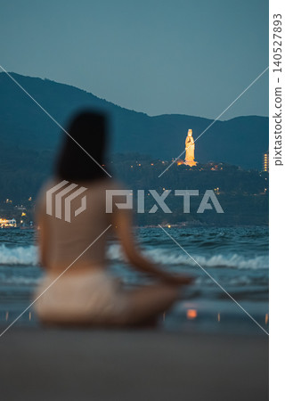 Woman meditating on beach shoreline with sea waves and Lady Buddha in Da Nang, Female practicing mindfulness by ocean at sunset with coastal mountains Woman meditating on beach shoreline with sea waves and Lady Buddha in Da Nang, Female practicing mindfulness by ocean at sunset with coastal mountains 140527893