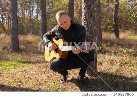Blonde man playing string guitar outdoors in autumn forest. Concept of sound therapy, mental health and wellness rituals. Calmness tranquility audio-sensory practices. Aura farming energy Blonde man playing string guitar outdoors in autumn forest. Concept of sound therapy, mental health and wellness rituals. Calmness tranquility audio-sensory practices. Aura farming energy 140527960