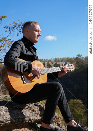 Portrait of smiling caucasian artist plays wooden acoustic guitar in autumnal park. Young songwriter plays string musical instrument hobby outside in nature fall time. Audio music healing Portrait of smiling caucasian artist plays wooden acoustic guitar in autumnal park. Young songwriter plays string musical instrument hobby outside in nature fall time. Audio music healing 140527965