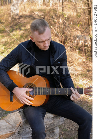 Beautiful blonde man playing acoustic guitar and singing relaxing enjoying outdoors on sunny autumn day. Artist learning and practicing playing musical instrument. Fall leaves autumnal 140527983