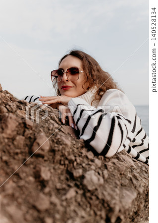 Woman sunglasses sweater leaning on a coastal rock while looking at the sea during a peaceful autumn day outdoors Woman sunglasses sweater leaning on a coastal rock while looking at the sea during a peaceful autumn day outdoors 140528134
