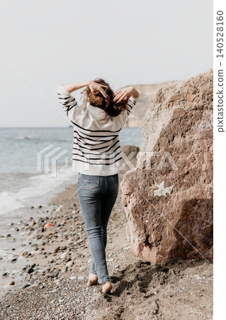 Beach woman sweater stands barefoot on a rocky shore overlooking the ocean while touching her curly hair in solitude Beach woman sweater stands barefoot on a rocky shore overlooking the ocean while touching her curly hair in solitude 140528160