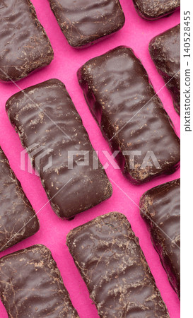 Dark chocolate covered rectangular candy bars with textured surface and slight imperfections, arranged diagonally on a vibrant pink background, close up, overhead view vertical photo Dark chocolate covered rectangular candy bars with textured surface and slight imperfections, arranged diagonally on a vibrant pink background, close up, overhead view vertical photo 140528455