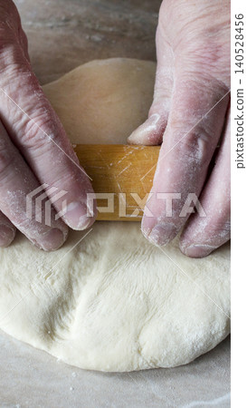 Hands rolling out fresh raw dough with wooden rolling pin, preparing culinary creation, close-up view of baking process, cooking preparation kitchen activity vertical photo 140528456