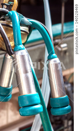 Close-up of modern milking machine teat cups with teal rubber liners and connecting hoses, highlighting dairy farm technology and clean industrial design of equipment vertical photo Close-up of modern milking machine teat cups with teal rubber liners and connecting hoses, highlighting dairy farm technology and clean industrial design of equipment vertical photo 140528469