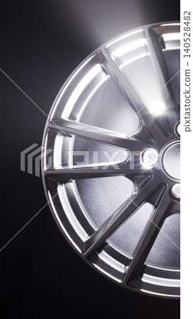 Close-up view of shiny metallic car wheel rim with bright reflections on spokes and polished surface against dark background, automotive part detail vertical photo Close-up view of shiny metallic car wheel rim with bright reflections on spokes and polished surface against dark background, automotive part detail vertical photo 140528482