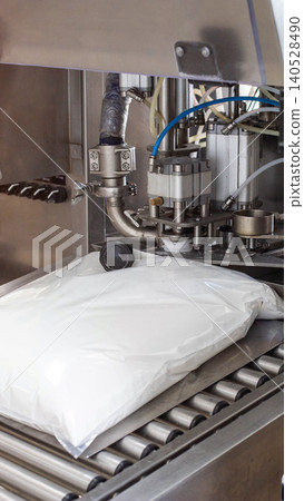 Automated filling and packaging machine at work, white powder product bag moving along a steel roller conveyor belt in a sterile food production facility, vertical photo Automated filling and packaging machine at work, white powder product bag moving along a steel roller conveyor belt in a sterile food production facility, vertical photo 140528490