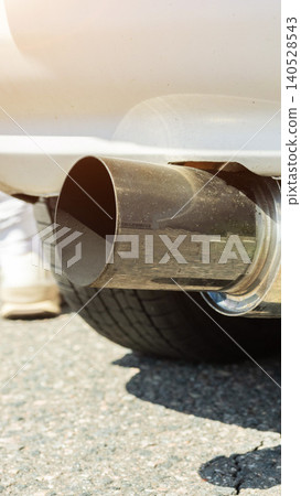Close-up vertical shot of robust car exhaust pipe, metallic finish, intricate detail of automotive component, part of tire on asphalt ground, emphasizing vehicle performance tuning concept. 140528543