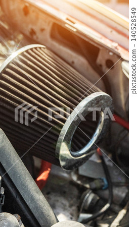 Performance air filter with metallic ring inside engine bay of modified vehicle, visible wires and hoses, bright lens flare from daylight, close up of tuning component, vertical orientation Performance air filter with metallic ring inside engine bay of modified vehicle, visible wires and hoses, bright lens flare from daylight, close up of tuning component, vertical orientation 140528549