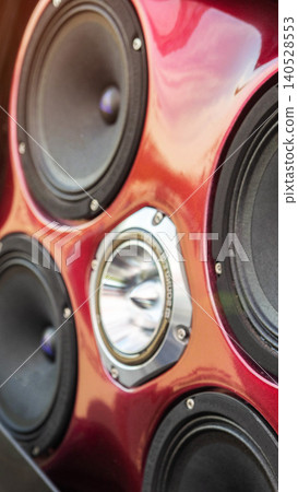 Close-up view of multiple car audio speakers with central reflective tweeter installed on custom glossy red panel, vertical photo capturing detail of sound system enhancement for vehicle tuning 140528553