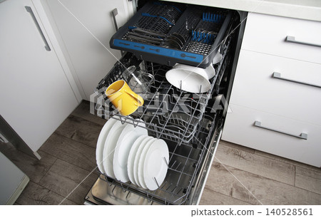 Modern built-in dishwasher open door showing upper and lower racks full of dirty dishes, cutlery, plates, and mugs ready for washing cycle Modern built-in dishwasher open door showing upper and lower racks full of dirty dishes, cutlery, plates, and mugs ready for washing cycle 140528561