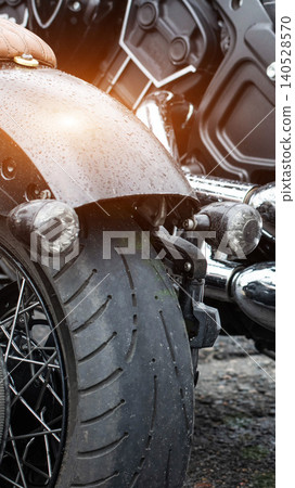 Close up rear section custom motorcycle with leather seat, dark fender, spoked wheel. Water droplets cover surfaces, highlighting detail of vehicle and showing effects of weather. 140528570