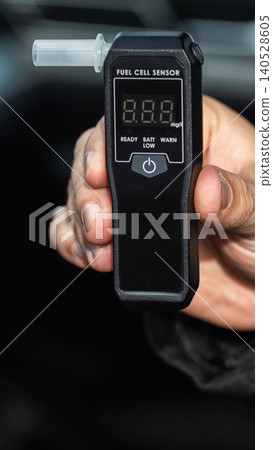Person hand holding black digital breathalyzer with clear mouthpiece and fuel cell sensor display showing zeros, ready status for alcohol testing, device for responsible driving vertical photo Person hand holding black digital breathalyzer with clear mouthpiece and fuel cell sensor display showing zeros, ready status for alcohol testing, device for responsible driving vertical photo 140528605