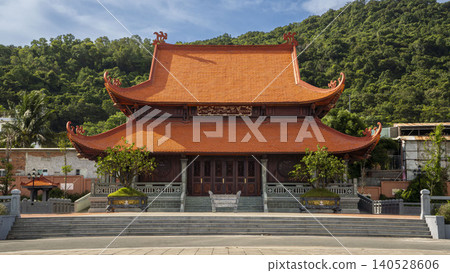 Magnificent Ho Chi Minh memorial temple with traditional double-tiered orange tiled roof and ornate wooden carvings, set against lush green hills in Vietnam. Magnificent Ho Chi Minh memorial temple with traditional double-tiered orange tiled roof and ornate wooden carvings, set against lush green hills in Vietnam. 140528606