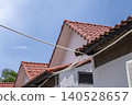 A low-angle shot looking up at overlapping red ceramic tiled rooftops of a residential building against a vivid blue sky. Cables run diagonally across the frame. 140528657
