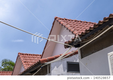 A low-angle shot looking up at overlapping red ceramic tiled rooftops of a residential building against a vivid blue sky. Cables run diagonally across the frame. A low-angle shot looking up at overlapping red ceramic tiled rooftops of a residential building against a vivid blue sky. Cables run diagonally across the frame. 140528657