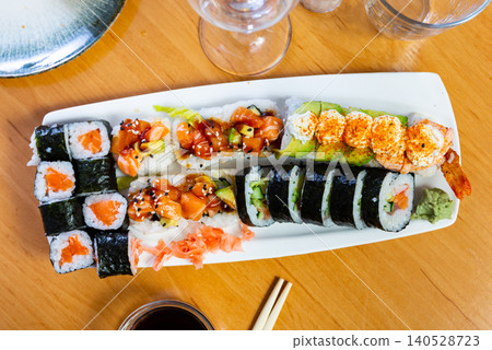 Assorted different types of maki, uramaki, with salmon, served with bowl of soy sauce on plate in restaurant Assorted different types of maki, uramaki, with salmon, served with bowl of soy sauce on plate in restaurant 140528723