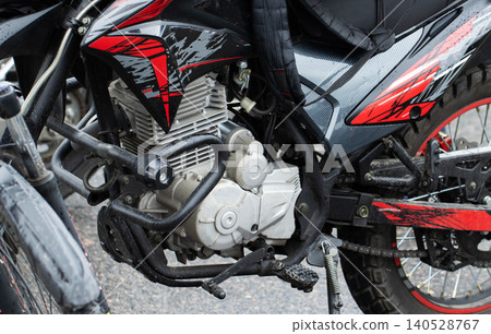 Close up view of dirt bike engine and frame details, showcasing protective crash bars, footpegs, and chain mechanism, with vibrant red and gray graphic design on black fairing, hint of off road Close up view of dirt bike engine and frame details, showcasing protective crash bars, footpegs, and chain mechanism, with vibrant red and gray graphic design on black fairing, hint of off road 140528767