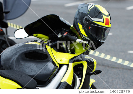 Motorcycle with vibrant neon yellow and black racing helmet parked outdoors on wet asphalt surface showing water droplets after rain 140528779