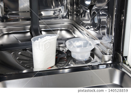 Dishwasher interior view showing white dishwasher salt crystals in measuring cup and plastic funnel placed in salt dispenser Dishwasher interior view showing white dishwasher salt crystals in measuring cup and plastic funnel placed in salt dispenser 140528859