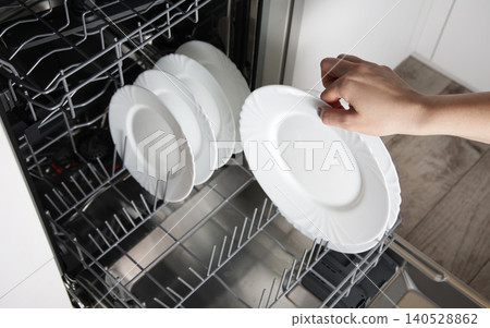 Person hand placing clean white dish into modern dishwasher appliance, kitchen chore completion, household efficiency device for clean dishes 140528862